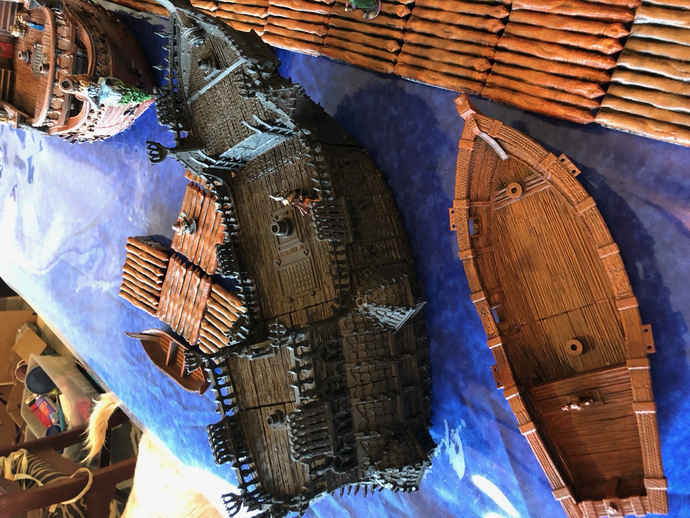 A wooden ship moored on blue water beneath a stone castle wall, built from painted tabletop terrain.