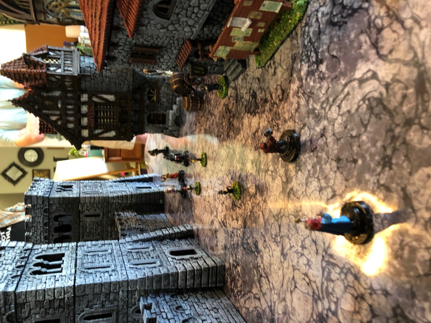 A cobbled lane between tall stone buildings leading to a tower, with a miniature walking it.